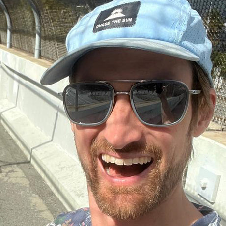 Man wearing sunglasses and a light blue cap with 'Chase the Sun' text, outdoors.