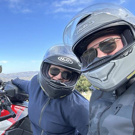 Two people wearing motorcycle helmets with a scenic background