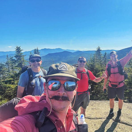 Four hikers on a mountain top with clear blue sky and trees in the background