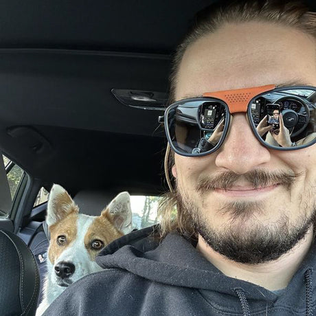 Man wearing large sunglasses with a dog in the background inside a car