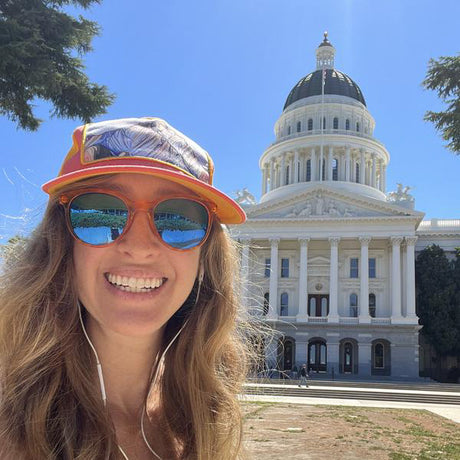 Person wearing sunglasses and a cap with the California State Capitol building in the background