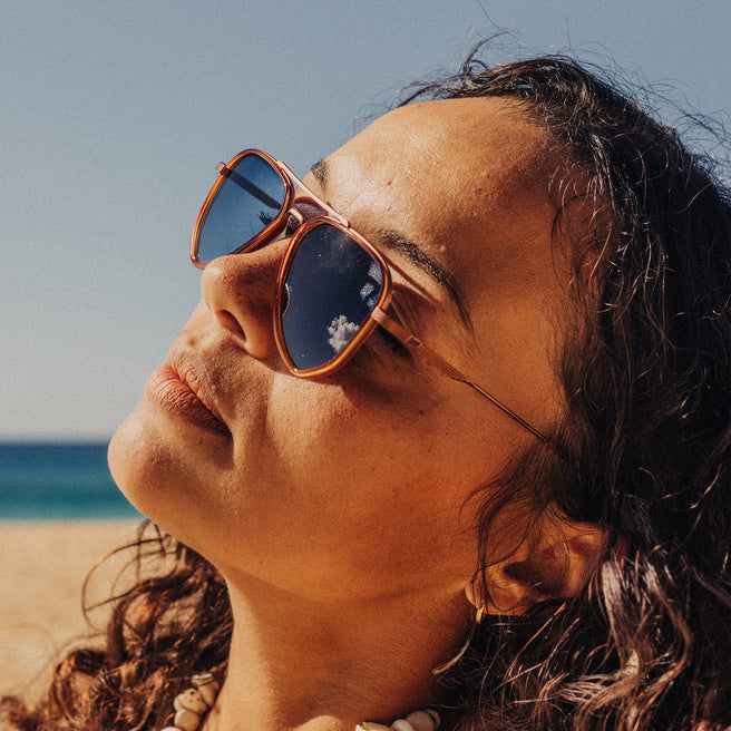 Woman wearing sunglasses with a beach and blue sky in the background