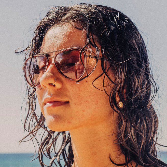 Woman wearing sunglasses with wet hair against a beach background