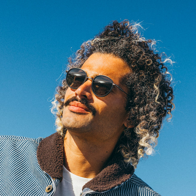 Man with sunglasses and curly hair against a clear blue sky