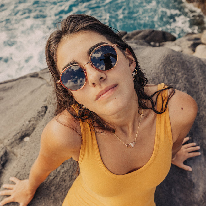 Woman wearing sunglasses and a yellow tank top by the ocean