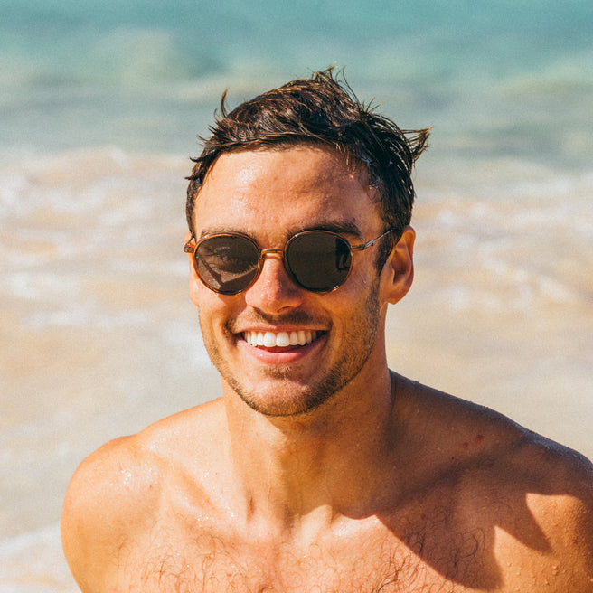 Man wearing sunglasses on a beach with clear blue water in the background