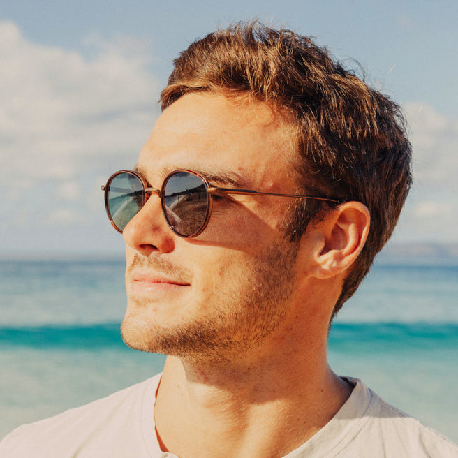Man wearing sunglasses with a beach and blue sky in the background