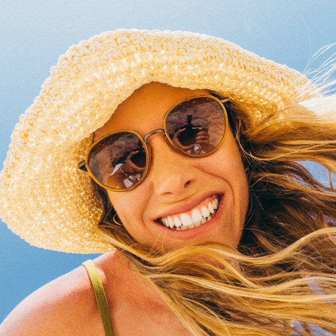 Woman wearing a straw hat and sunglasses with a clear blue sky background