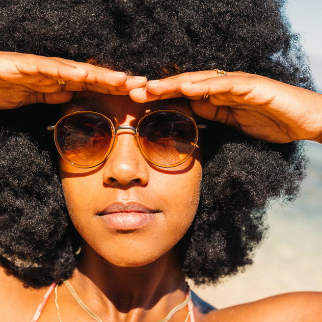 Woman wearing sunglasses with hands on head, blurred background