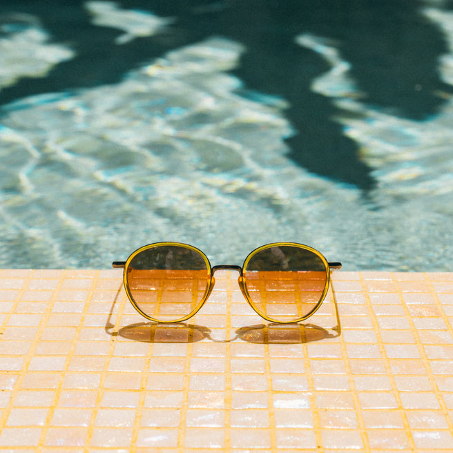 Yellow sunglasses on a poolside ledge with water and shadows in the background