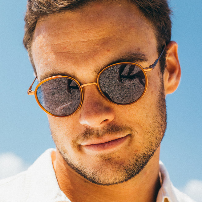 Man wearing round sunglasses with a clear blue sky background