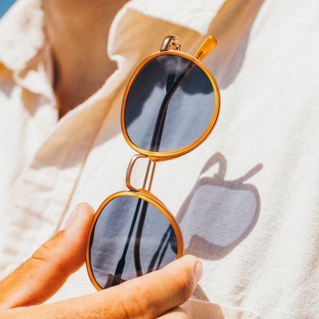 Person holding a pair of round sunglasses with gold frame and black lenses.