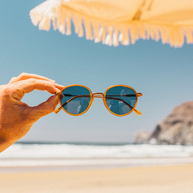 Sunglasses held up with a beach and sky in the background