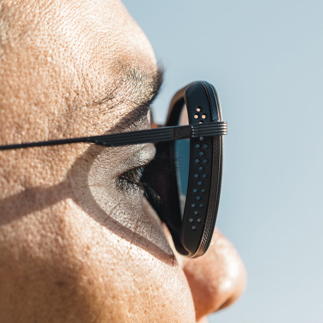 Close-up of a person wearing black sunglasses with a clear blue sky background