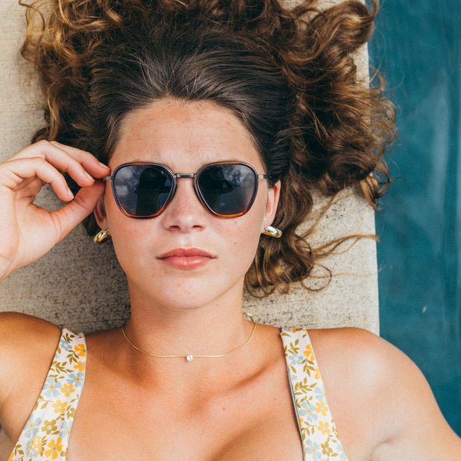 Woman wearing sunglasses and a floral dress by a poolside