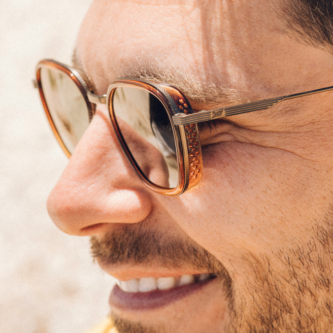 Close-up of a person wearing gold-framed sunglasses with a blurred background