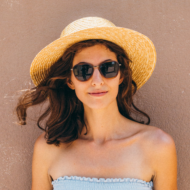 Woman wearing a straw hat and sunglasses against a beige background