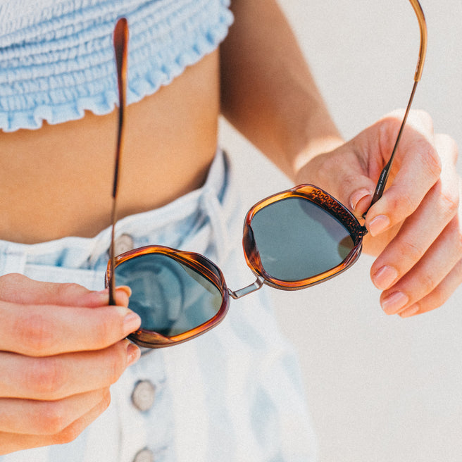 Person holding a pair of sunglasses with a blurred background