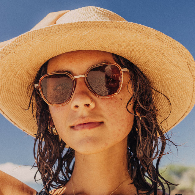 Person wearing a straw hat and sunglasses with a clear blue sky background