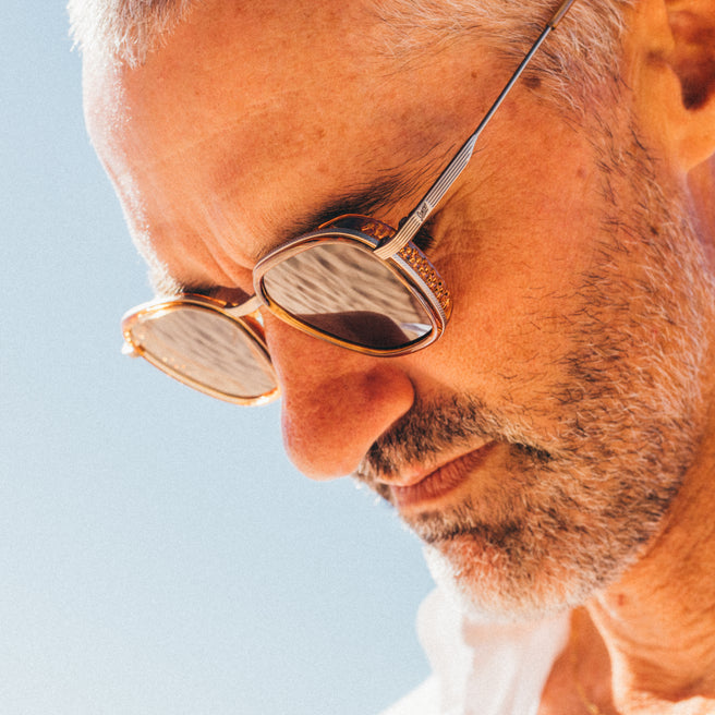 Close-up of a person wearing gold-rimmed sunglasses against a clear blue sky.