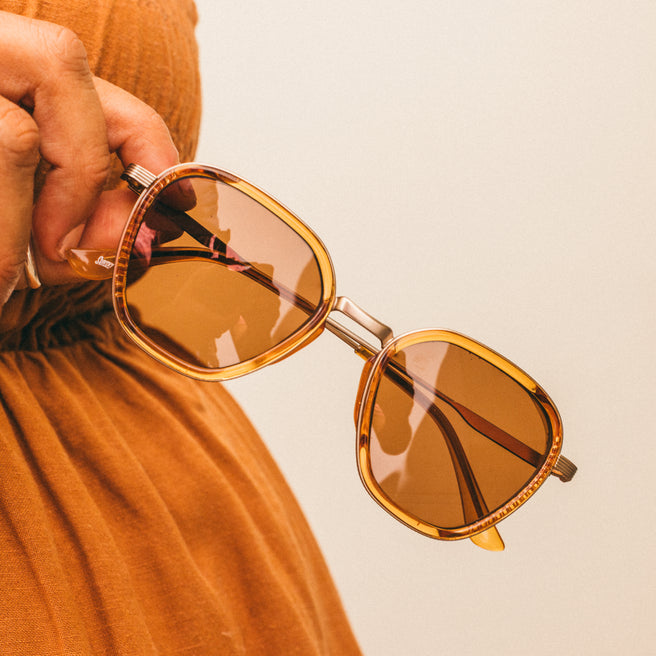 Person holding a pair of sunglasses with a neutral background