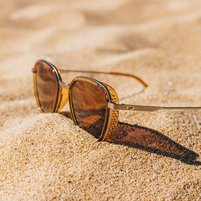 Gold-framed sunglasses on a sandy surface