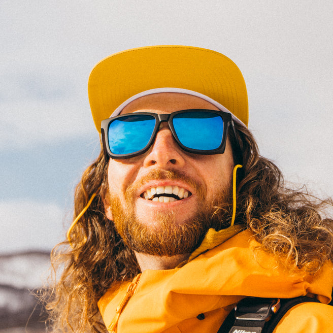 Man wearing a yellow cap and sunglasses with a blurred natural background