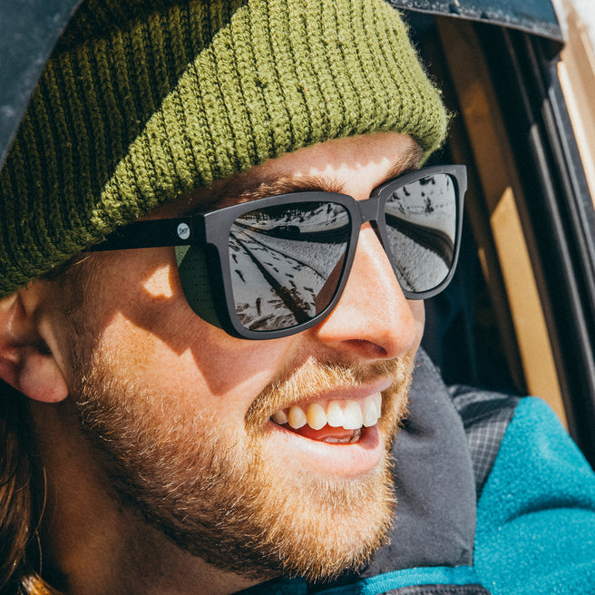 Man wearing sunglasses and a green beanie with a blurred natural background