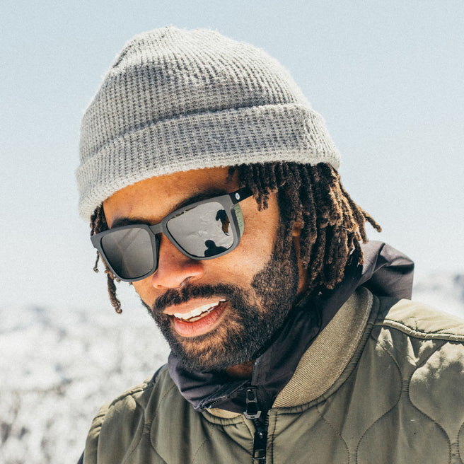 Man wearing sunglasses and a beanie outdoors with a blurred natural background