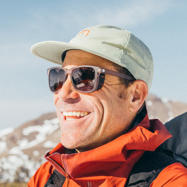 Man wearing sunglasses and a cap with mountains in the background