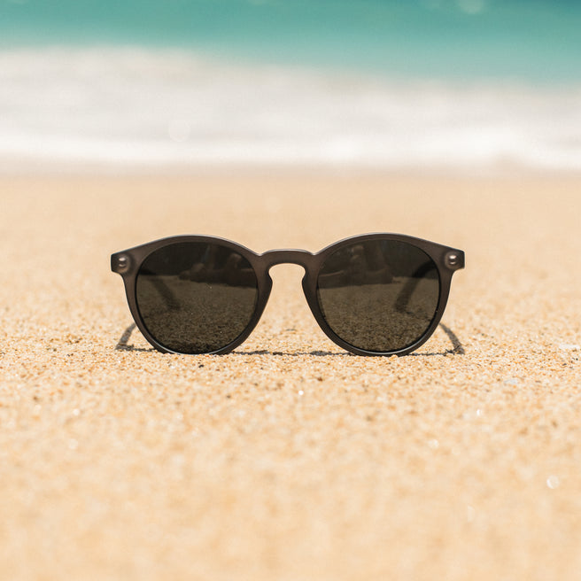Black sunglasses on a sandy beach with a blurred ocean background