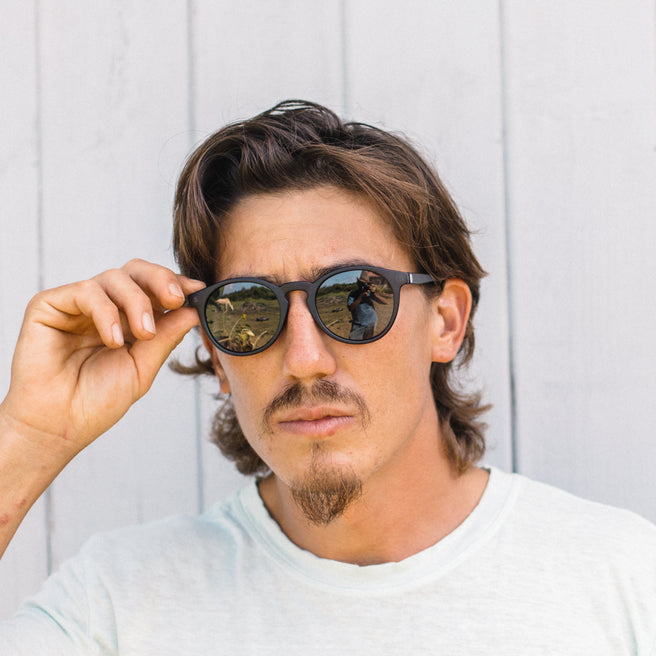Man holding sunglasses up to his face against a light background