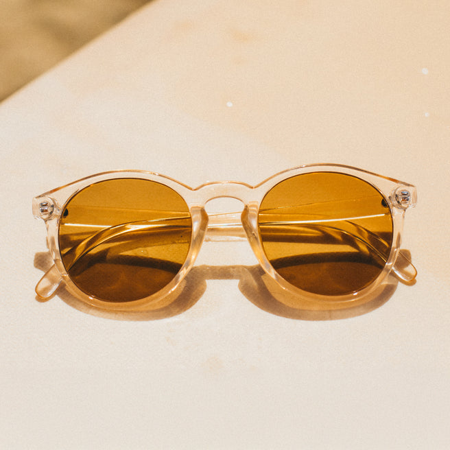 Round sunglasses with gold lenses on a beige surface