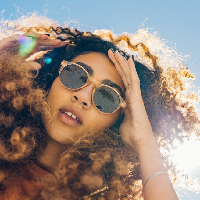 Woman with curly hair wearing sunglasses against a blue sky