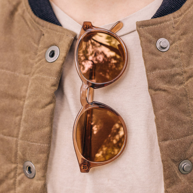 Brown sunglasses held against a person wearing a beige jacket.