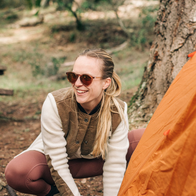 Woman in sunglasses and outdoor attire sitting next to a tree