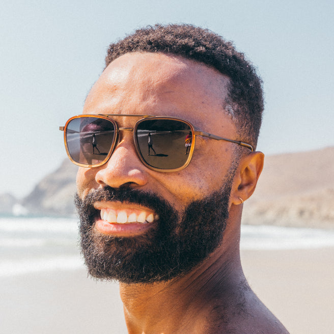 Man wearing sunglasses with a beach and mountain in the background