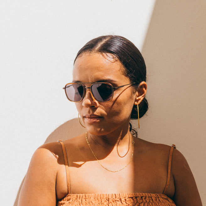 Woman wearing sunglasses and a brown top against a neutral background