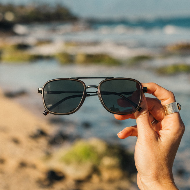 Person holding sunglasses with a blurred beach background