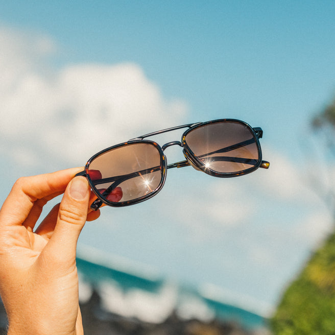 Hand holding sunglasses with a blurred outdoor background