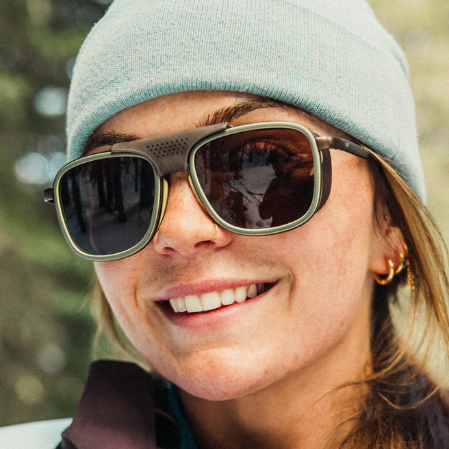Person wearing sunglasses and a beanie with a blurred natural background