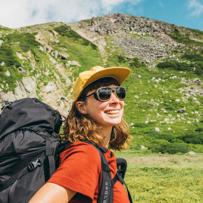 Person with a backpack and sunglasses standing in a mountainous landscape