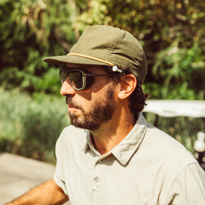 Man wearing a green cap and sunglasses with a blurred natural background