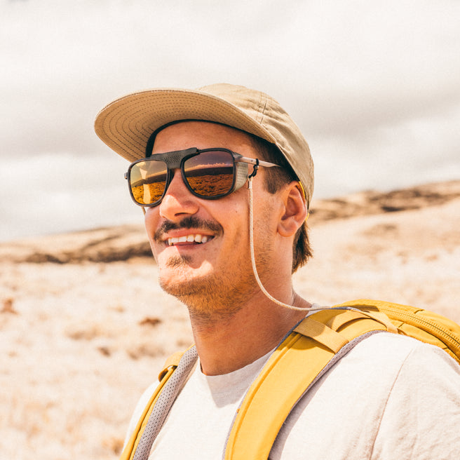 Man wearing a hat and sunglasses with a yellow backpack in a desert setting
