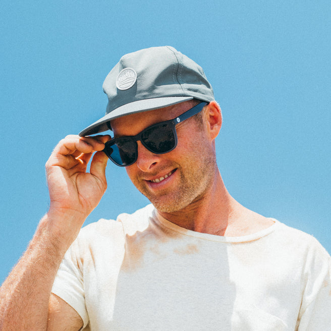 Man wearing a gray cap and sunglasses with a clear blue sky background