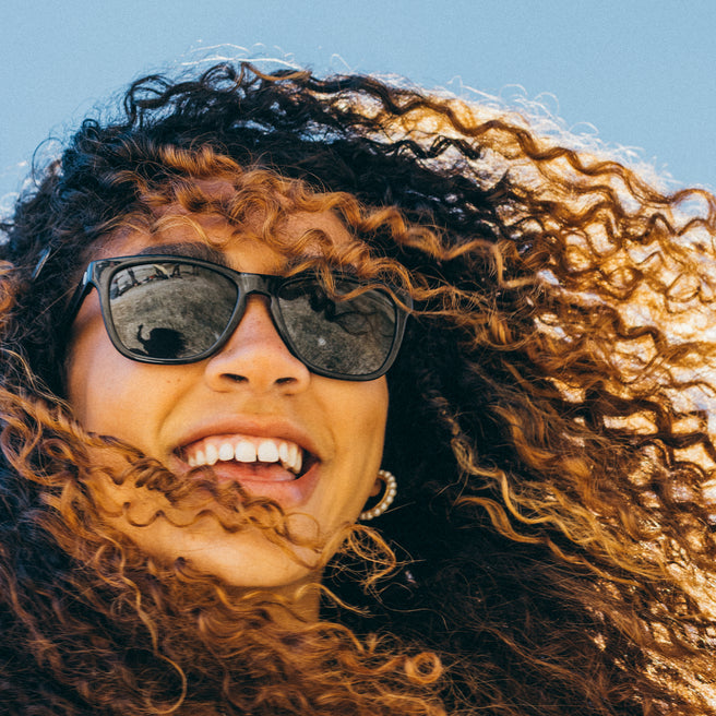 Person with curly hair wearing sunglasses against a blue sky