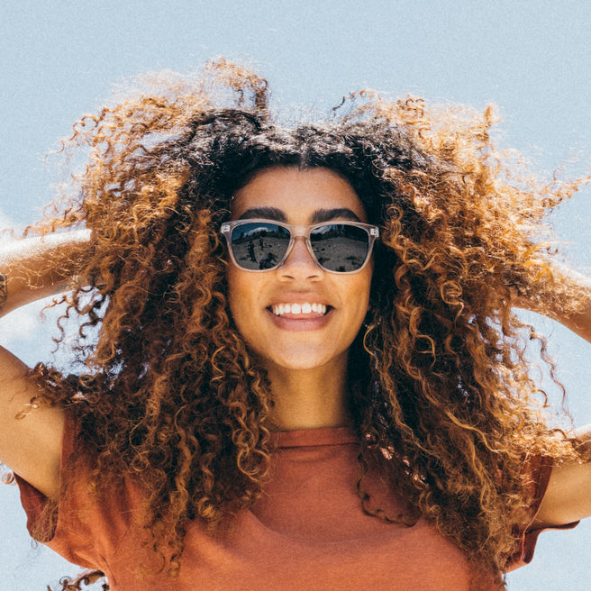 Woman with curly hair wearing sunglasses against a clear blue sky