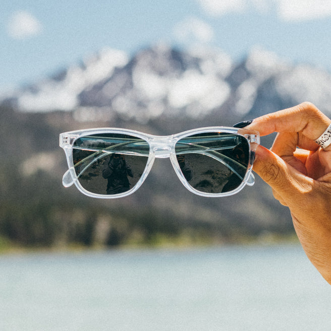 Person holding sunglasses with a mountain and lake background