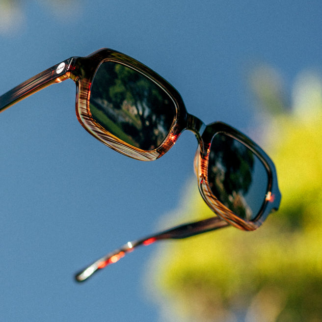 Sunglasses with reflective lenses against a blue sky and blurred greenery