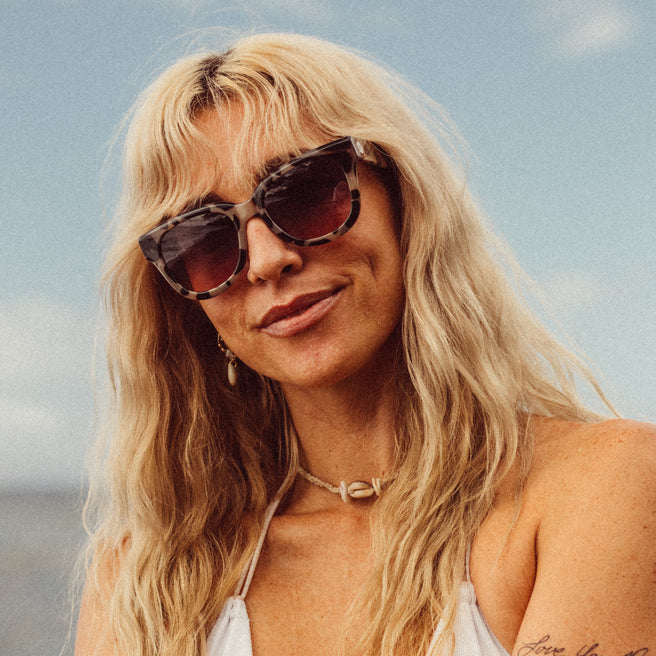 Woman with sunglasses and blonde hair against a blue sky.
